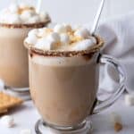 a prepared smores latte in a clear glass mug. There is a second one prepared but blurred in the background.