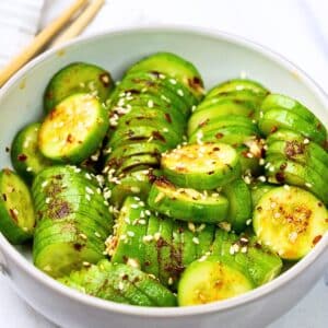 An aerial view of the prepared cucumber salad in a white bowl with a white background. The cucumbers have sesame seeds on them as a garnish.