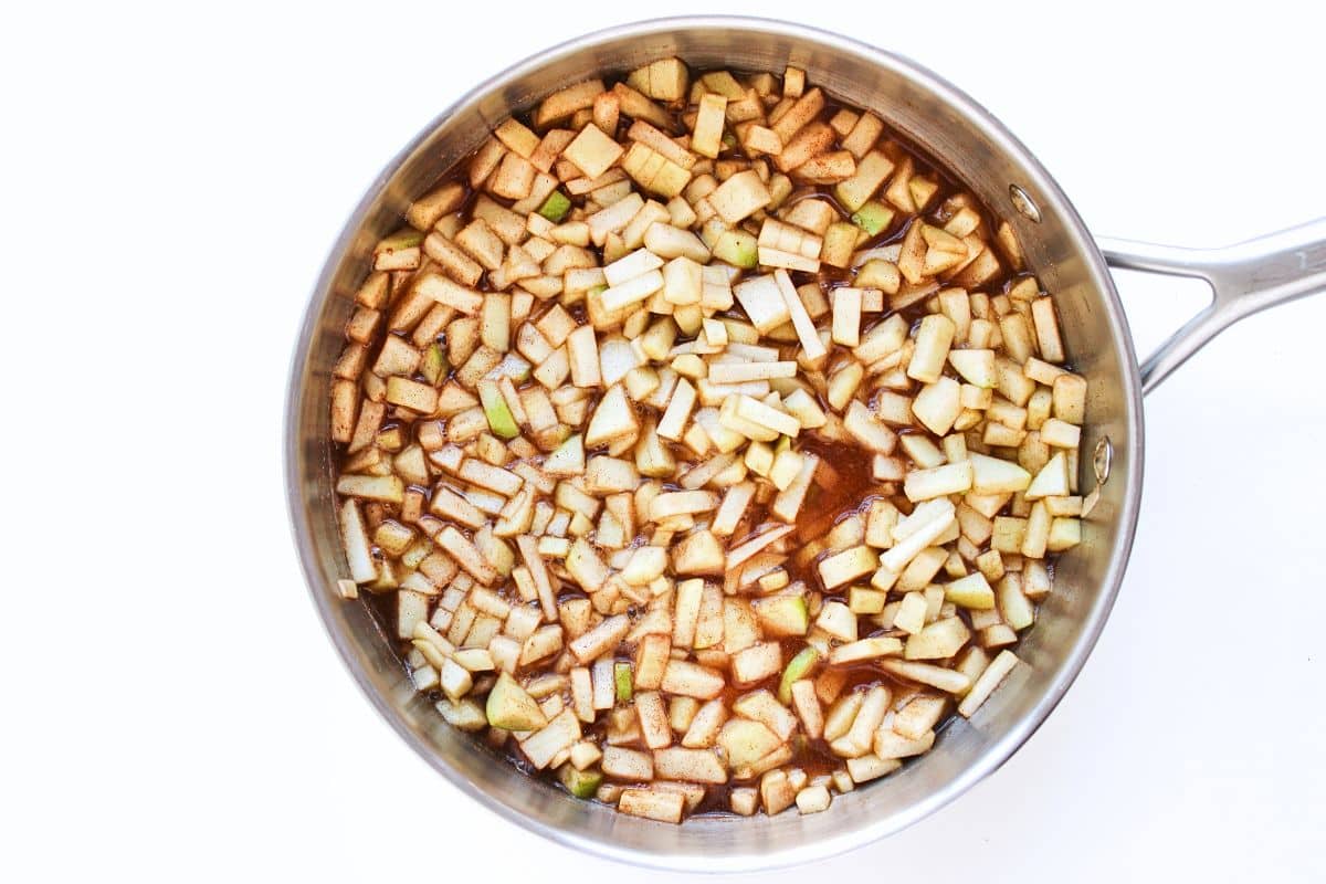 Apple pie filling mixture cooking in a large stainless steel pan.