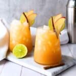 Two glasses of the finished mocktails. Both glasses are garnished with apple slices and a cinnamon stick. The glasses are on a gray slate.