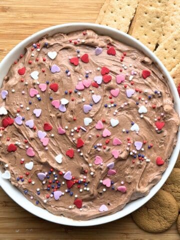 An overhead view of the prepared brownie batter dip in a white bowl. It is close up but you can see small amounts of graham crackers and fruit to right of the bowl.