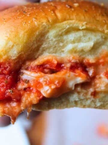 Close up view of one slider being held up. There is sauce, cheese and chicken dripping from the sandwich.