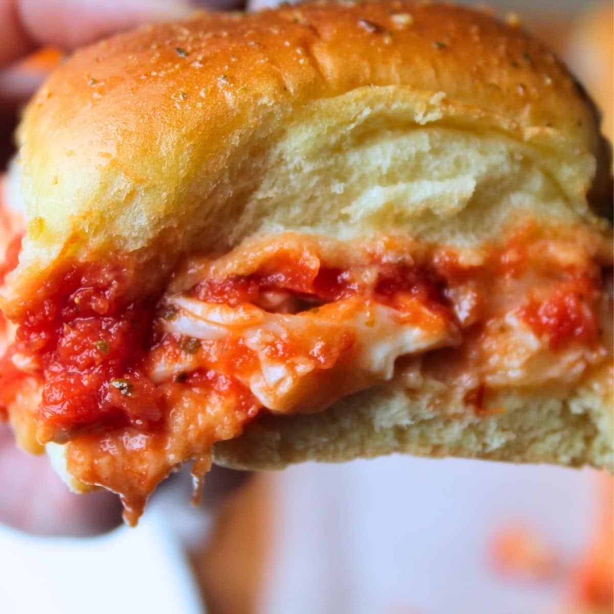 Close up view of one slider being held up. There is sauce, cheese and chicken dripping from the sandwich.