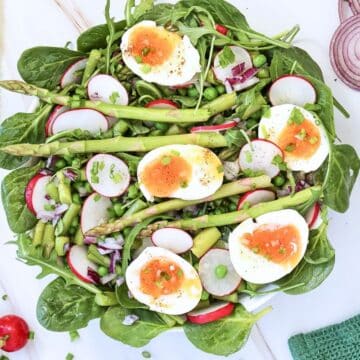 an overhead view of the prepared salad. It sits on a white tablecloth and there are chopped herbs scattered around the tablecloth.
