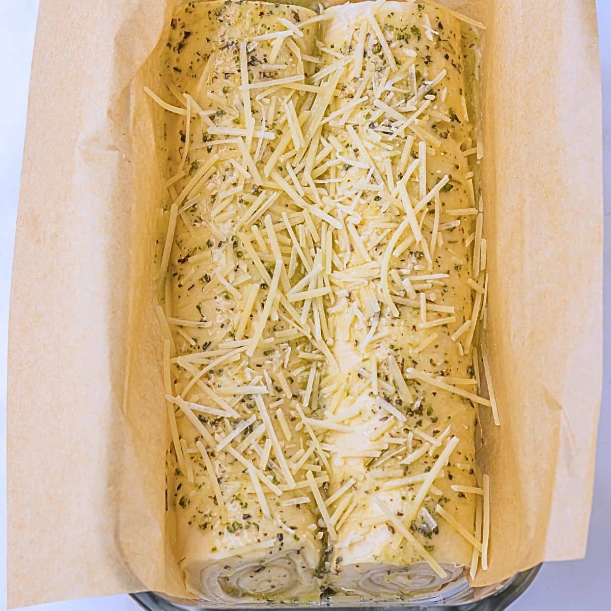 A close up of the two raw crescent doughs seasoned and topped with cheese in a loaf pan.
