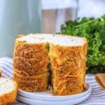 Several slices of the prepared bread on stacked on a white plate. There are fresh herbs behind it in the background.