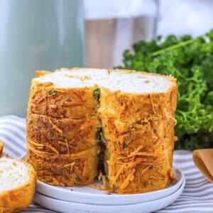 Several slices of the prepared bread on stacked on a white plate. There are fresh herbs behind it in the background.