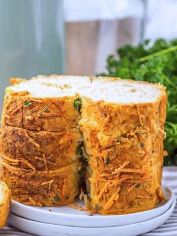 Several slices of the prepared bread on stacked on a white plate. There are fresh herbs behind it in the background.