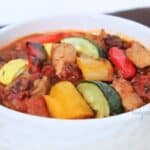 A close up of a white bowl filled with chunky vegetables atop chili.