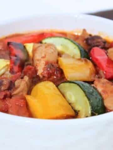 A close up of a white bowl filled with chunky vegetables atop chili.